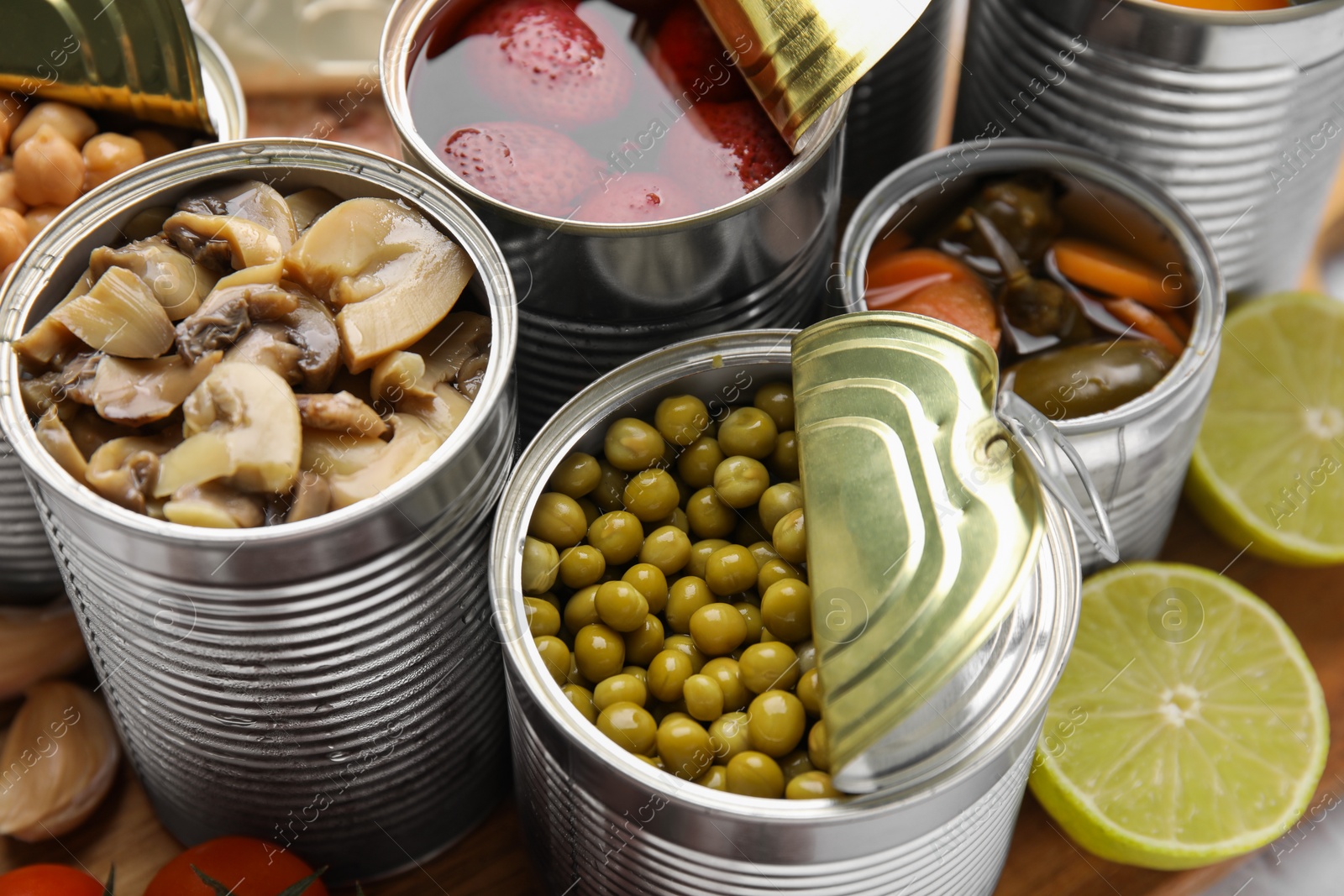 Photo of Open tin cans with different preserved products on wooden board, closeup