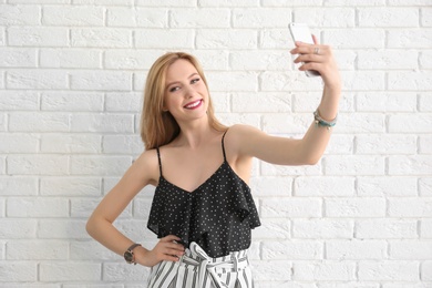 Photo of Attractive young woman taking selfie near brick wall