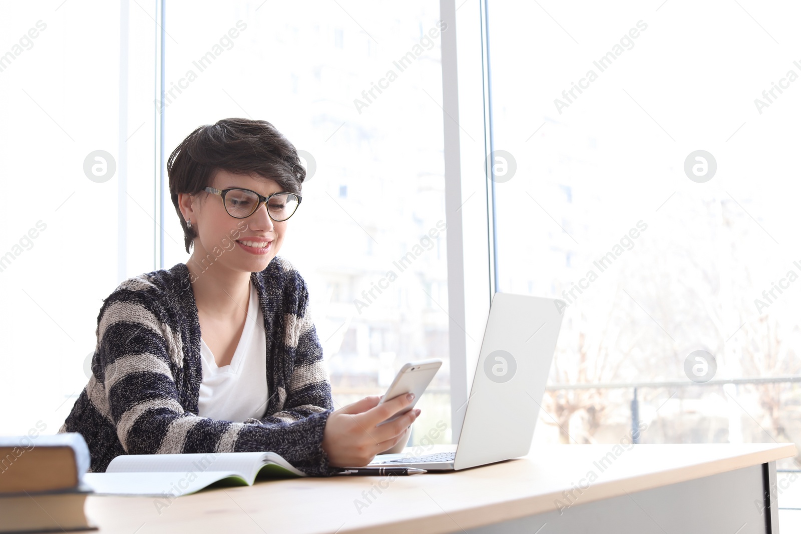 Photo of Young woman working with mobile phone ad laptop at desk. Home office