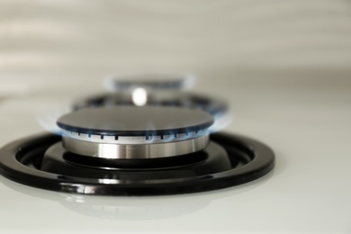 Photo of Gas burner with blue flame on modern stove, closeup. Space for text