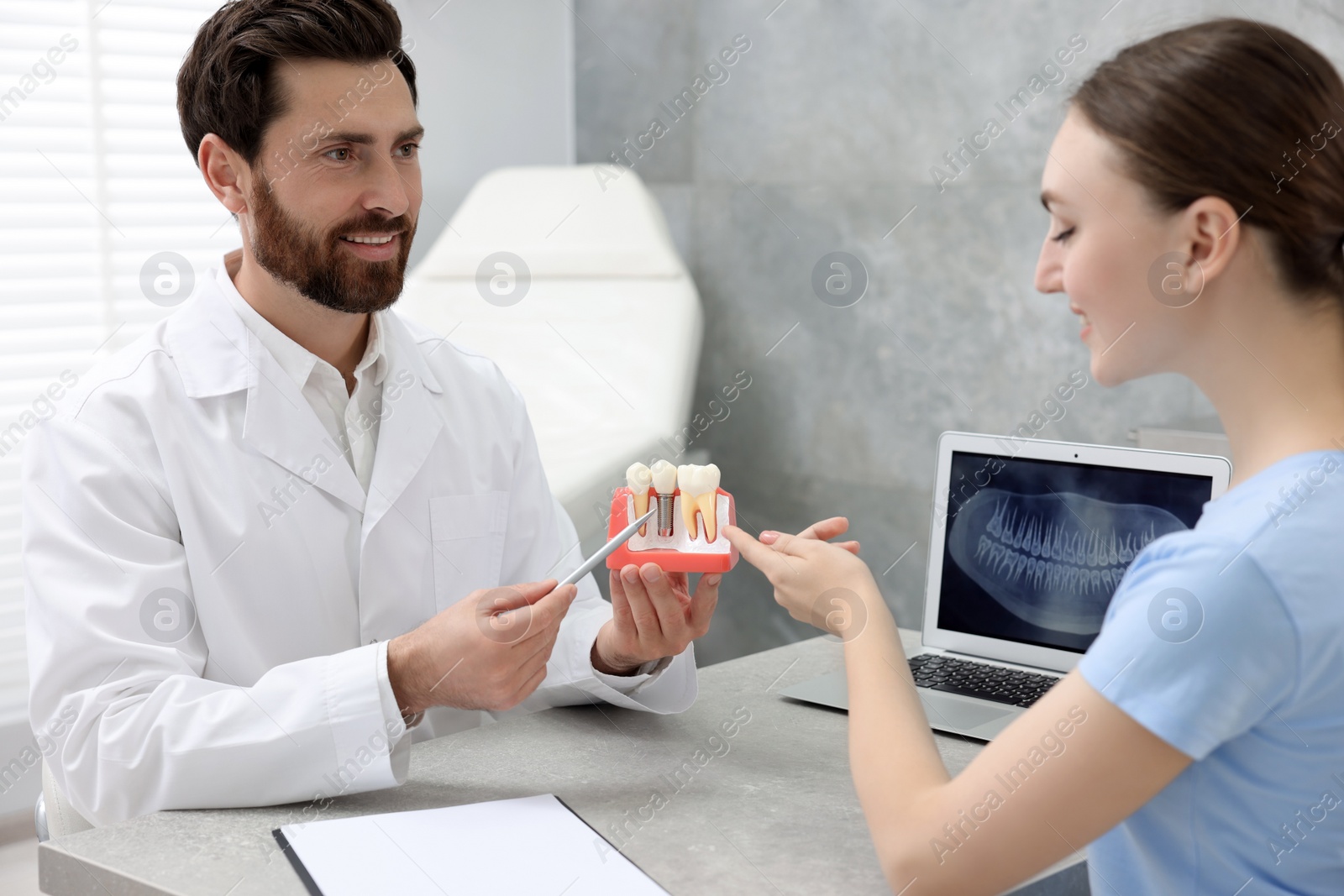 Photo of Doctor showing patient educational model of dental implant in clinic