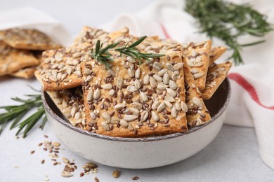 Photo of Cereal crackers with flax, sunflower, sesame seeds and rosemary in bowl on light table, closeup