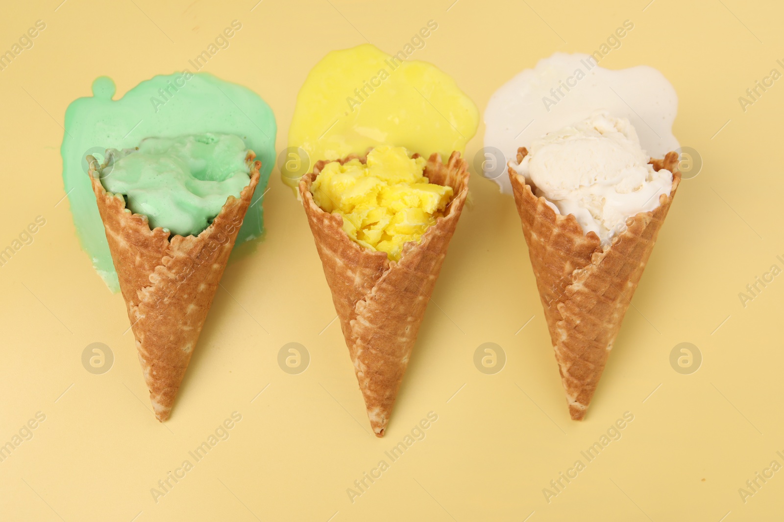 Photo of Melted ice cream in wafer cones on pale yellow background, flat lay