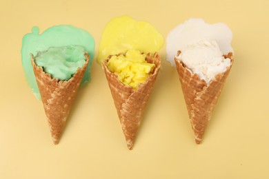 Photo of Melted ice cream in wafer cones on pale yellow background, flat lay