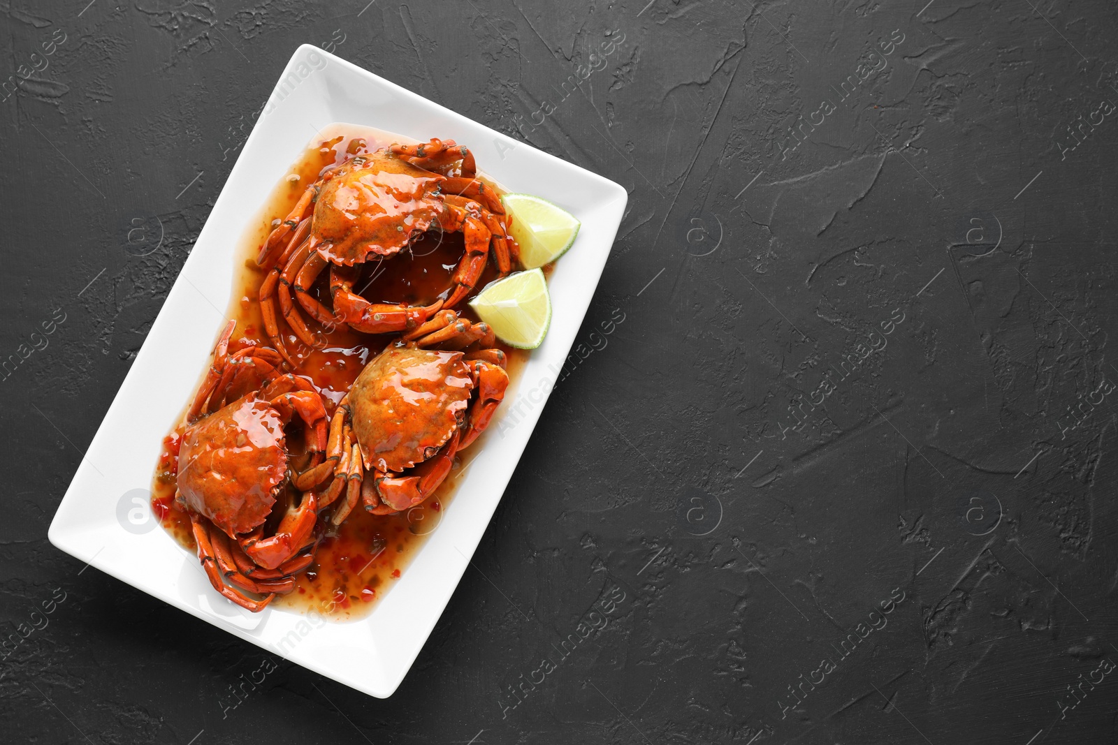 Photo of Delicious boiled crabs with sauce and lime on black textured table, top view. Space for text