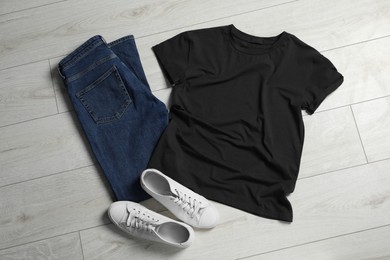 Photo of Stylish t-shirt, sneakers and jeans on white wooden background, flat lay
