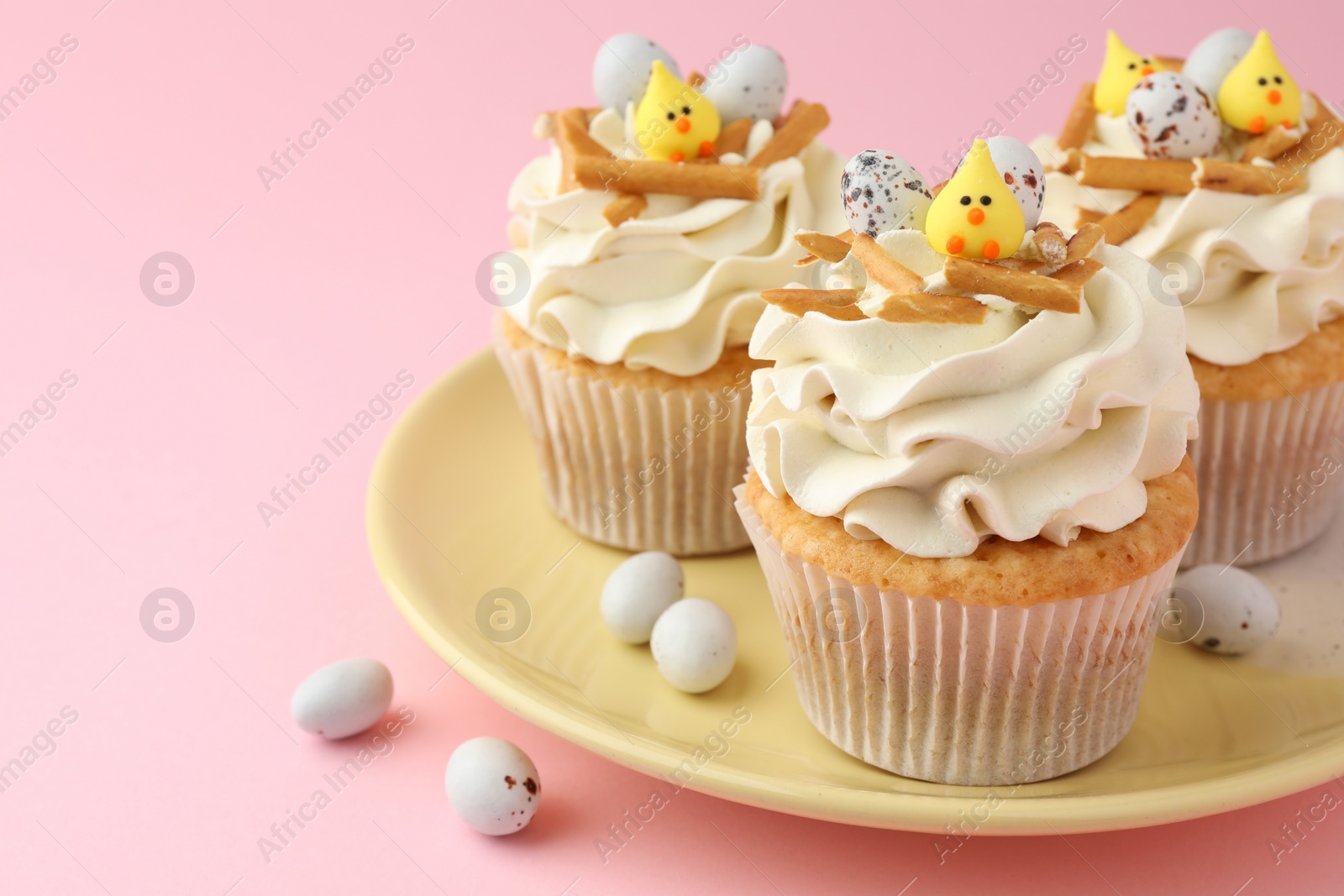 Photo of Tasty Easter cupcakes with vanilla cream and candies on pink background, closeup