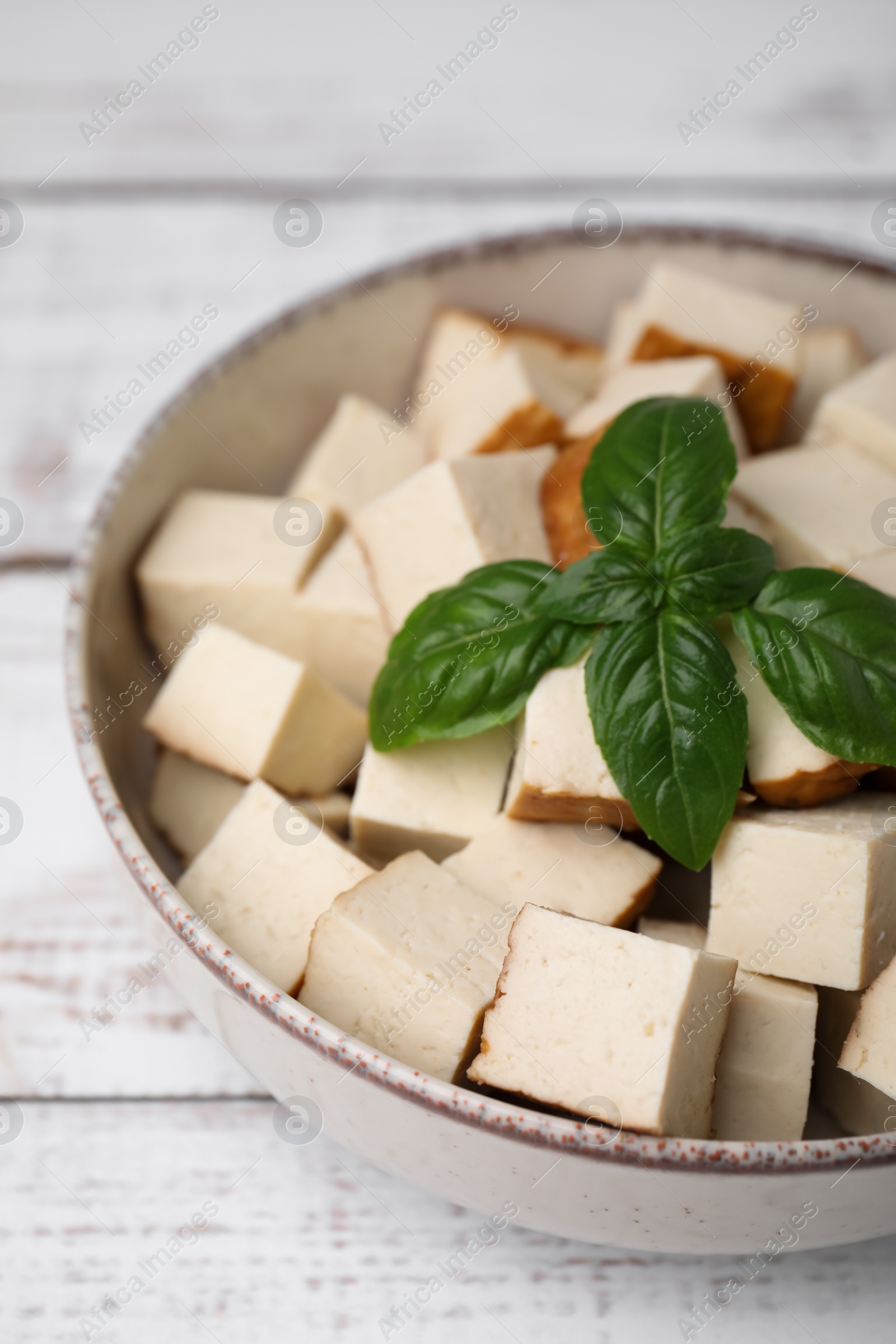 Photo of Bowl with delicious fried tofu and basil on white wooden table