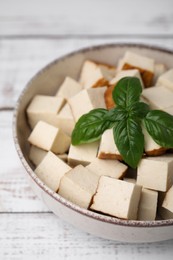 Bowl with delicious fried tofu and basil on white wooden table