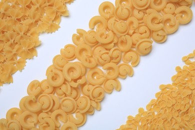 Photo of Different types of raw pasta on white background, flat lay