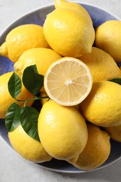 Fresh lemons and green leaves on light table, top view