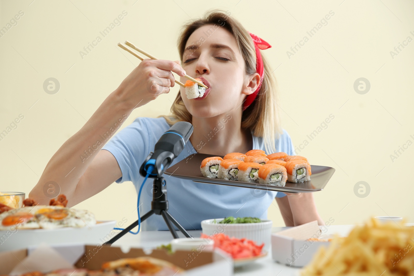 Photo of Food blogger eating in front of microphone at table against light background. Mukbang vlog