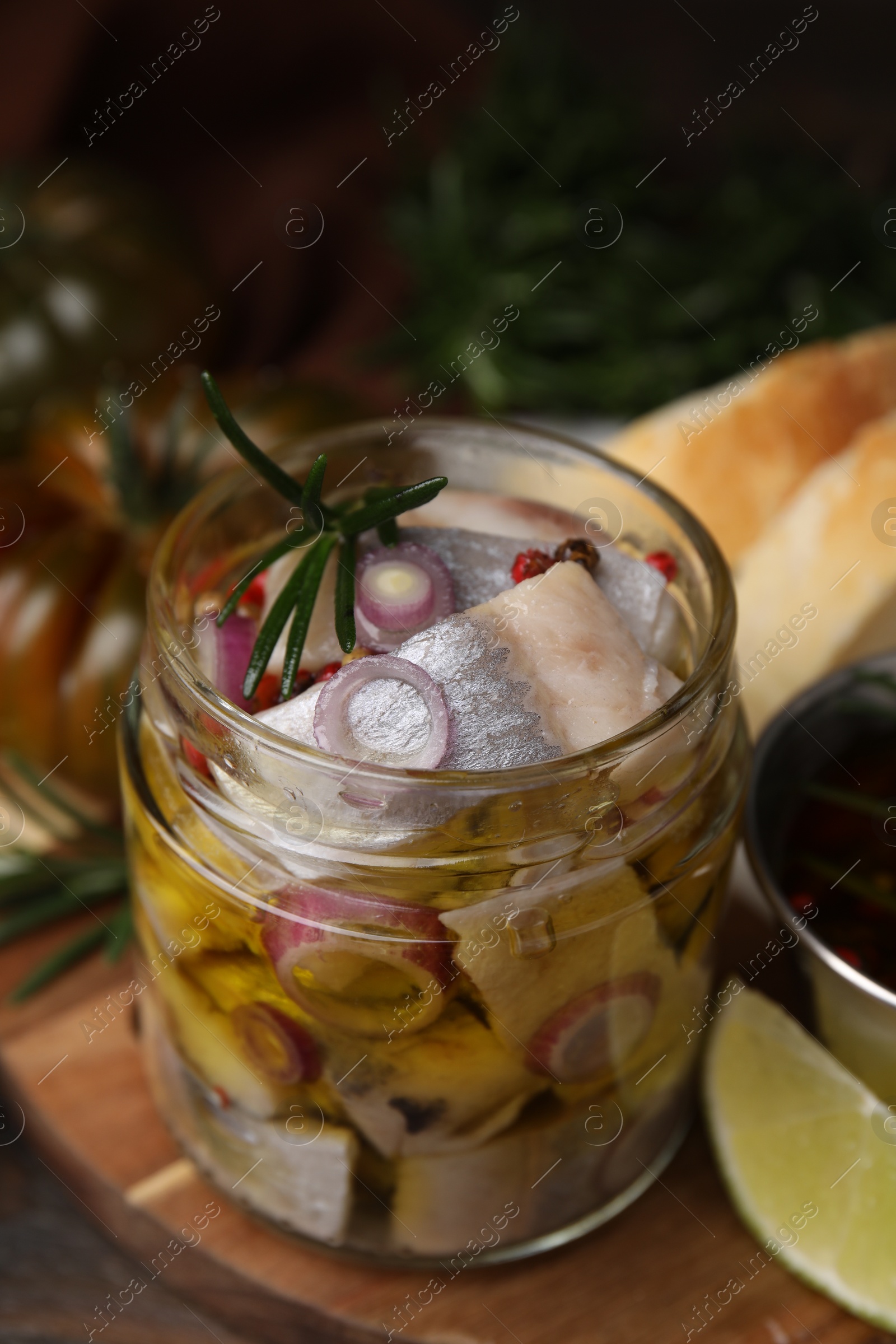 Photo of Tasty marinated fish with onion and rosemary in jar on wooden table, closeup