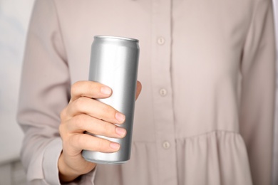 Woman holding aluminum can with beverage on blurred background, closeup. Space for design