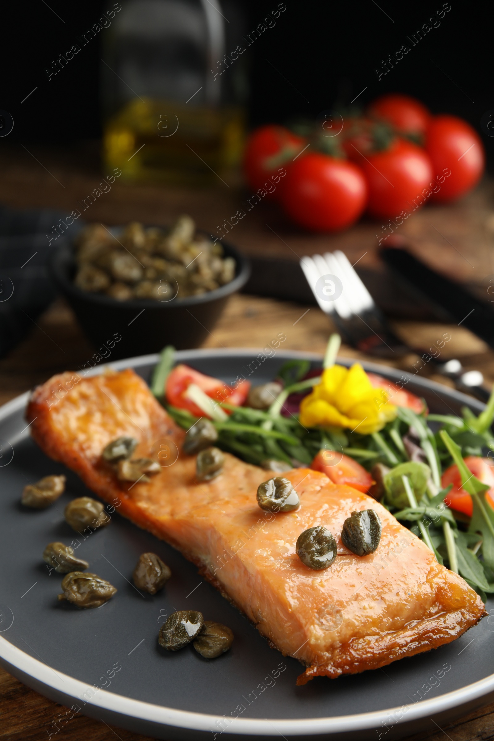 Photo of Tasty cooked salmon with capers and salad served on table, closeup