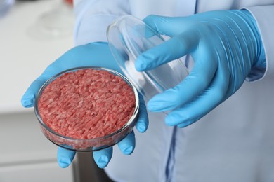 Scientist holding Petri dish with minced cultured meat in laboratory, closeup