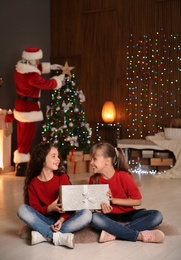 Photo of Little children with gift and Santa Claus decorating Christmas tree at home