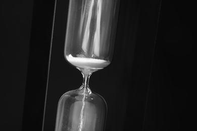 Photo of Hourglass with flowing sand on black background. Time management