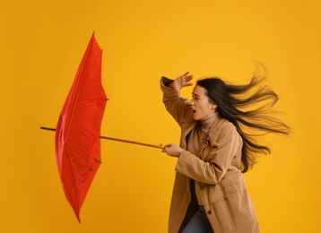 Photo of Emotional woman with umbrella caught in gust of wind on yellow background