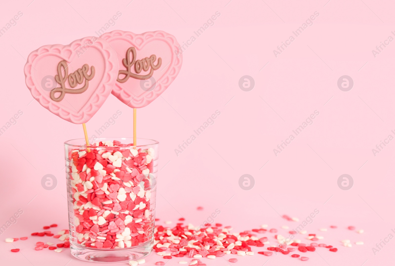 Photo of Chocolate heart shaped lollipops with word Love and sprinkles in glass on light pink background. Space for text