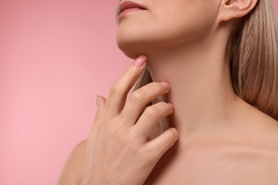 Woman touching her neck on pink background, closeup