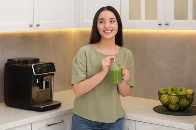 Beautiful young woman holding mason jar with delicious smoothie in kitchen