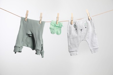 Cute baby clothes drying on washing line against white background