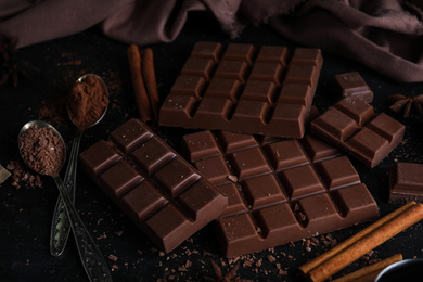 Photo of Tasty milk chocolate and spoons with cocoa powder on black table