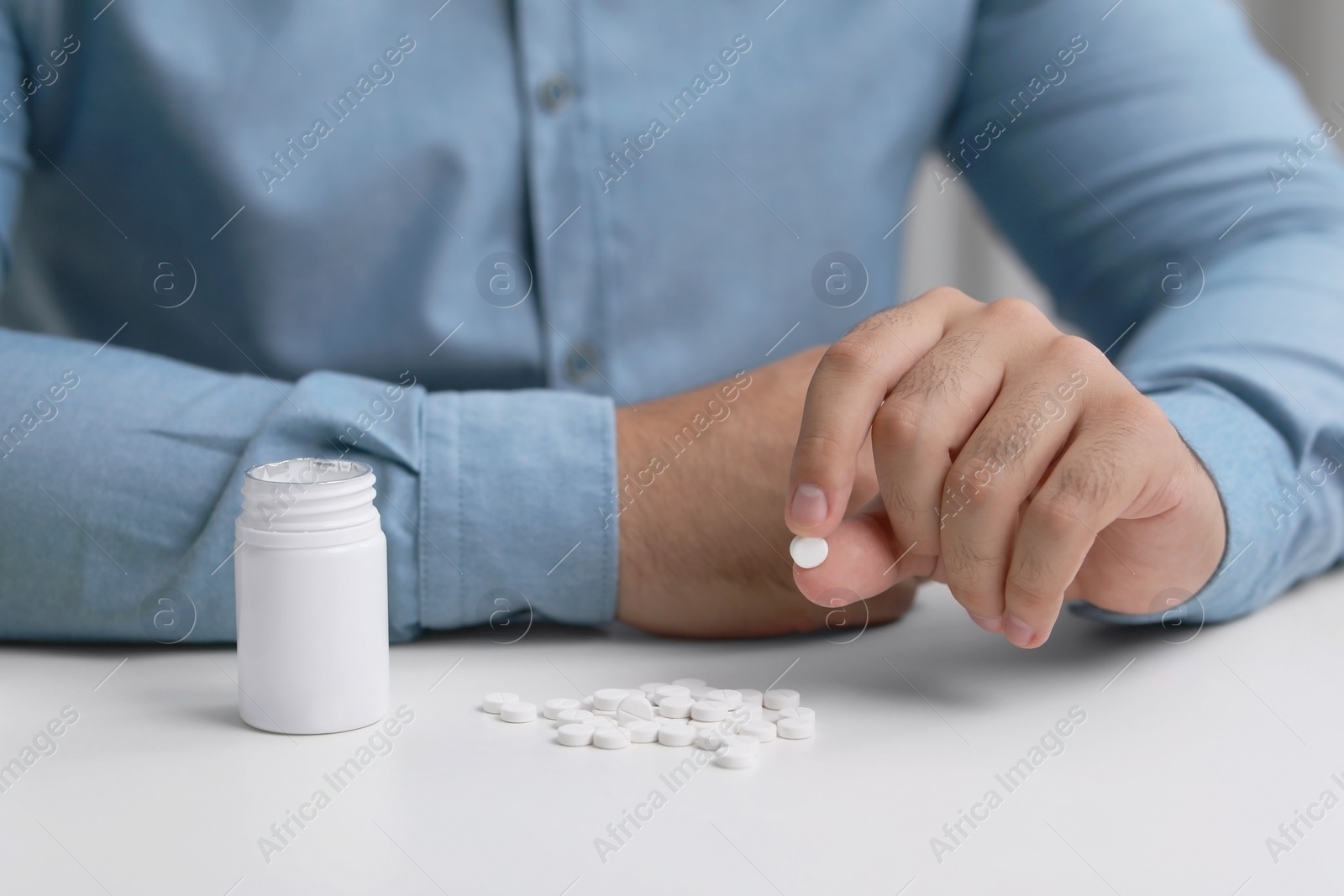 Photo of Man holding antidepressant pill at white table, closeup