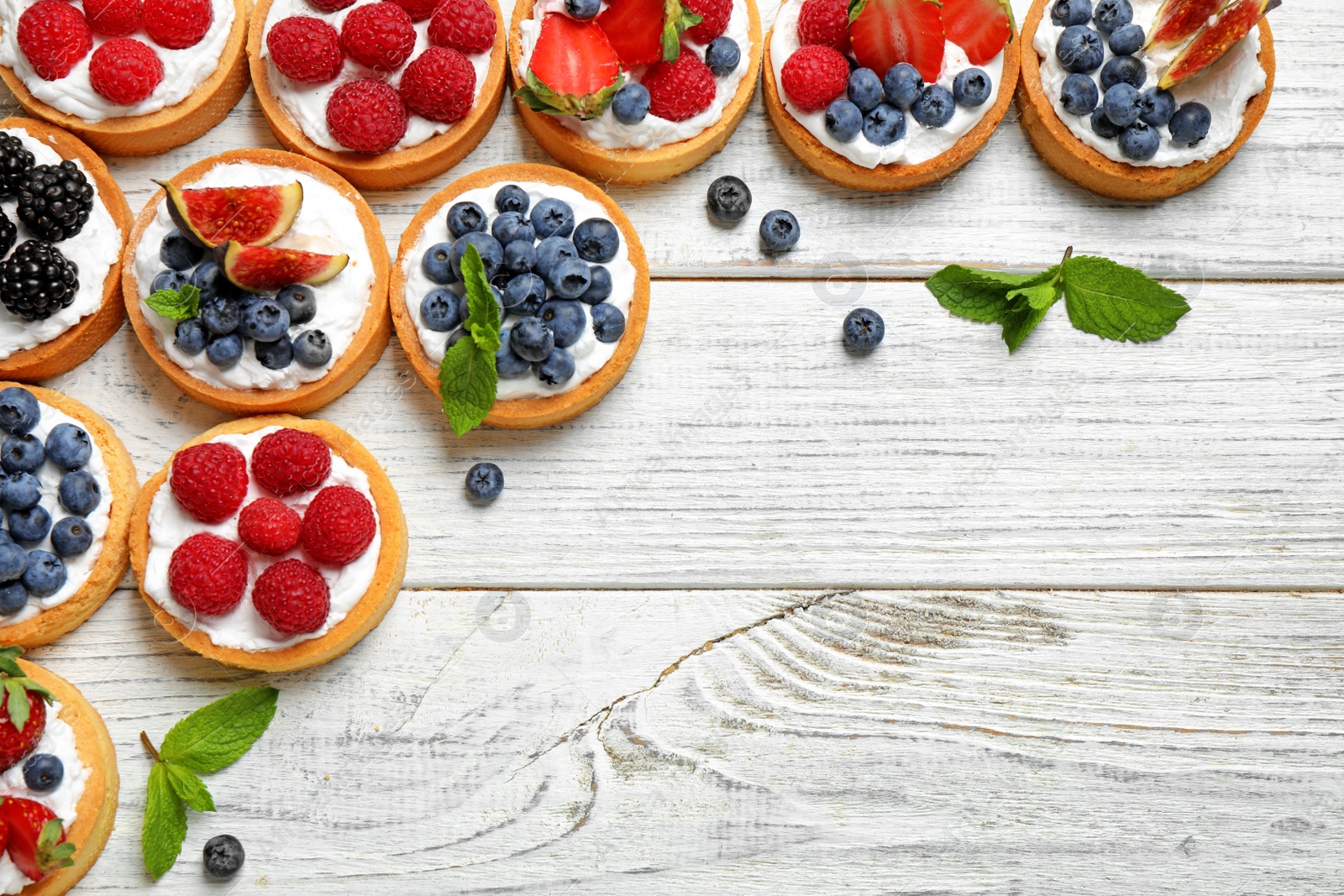 Photo of Different berry tarts on white wooden table, flat lay with space for text. Delicious pastries