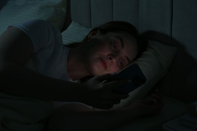 Photo of Woman using smartphone on bed at night. Internet addiction