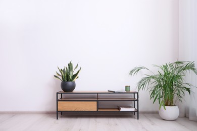Photo of Elegant room interior with wooden cabinet and beautiful houseplants near white wall