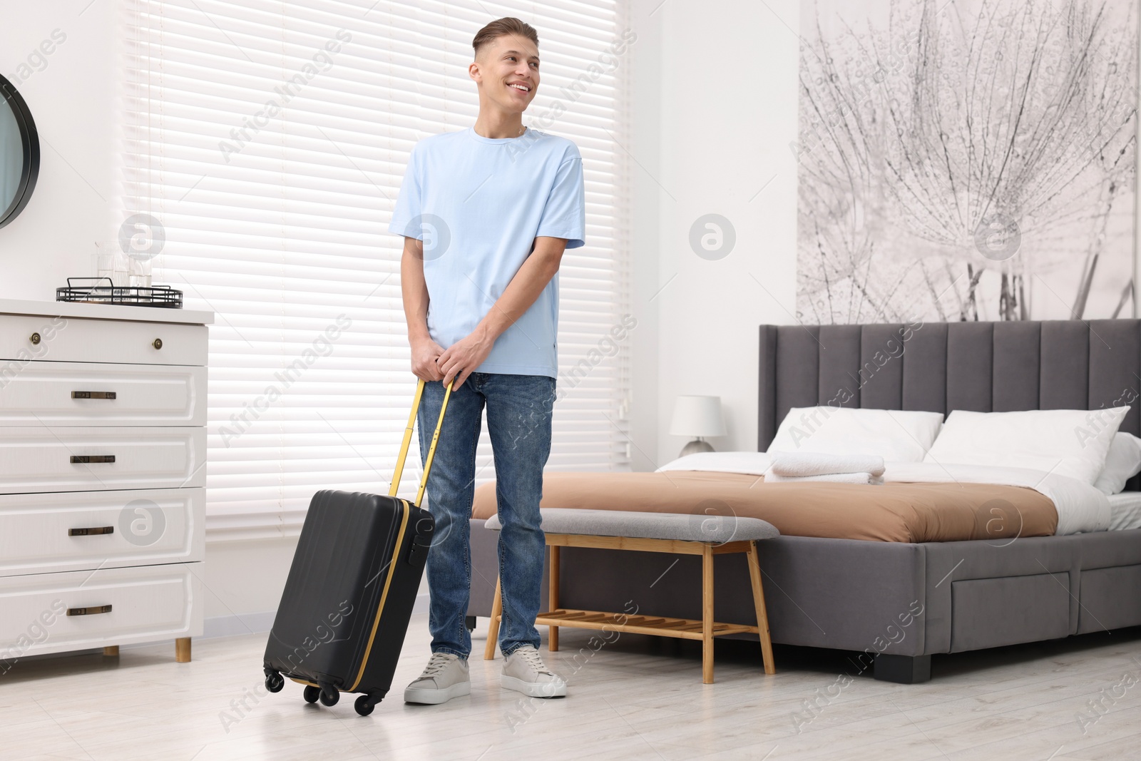 Photo of Smiling guest with suitcase exploring stylish hotel room