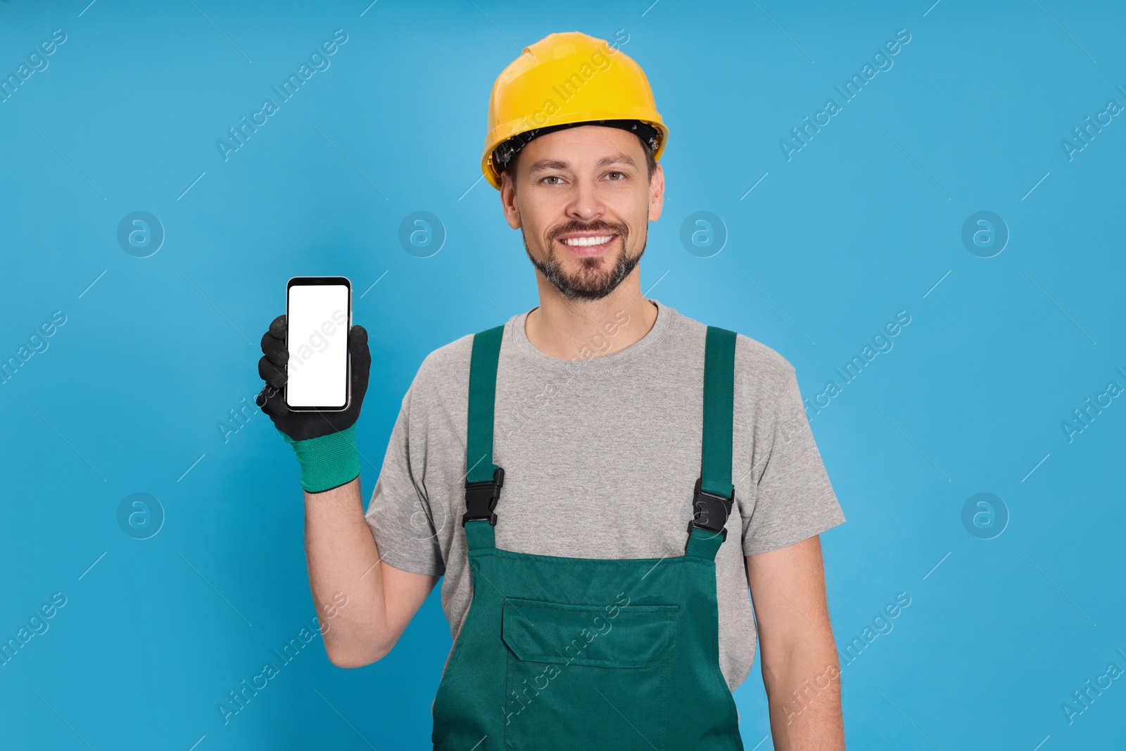 Photo of Professional repairman in uniform with phone on light blue background