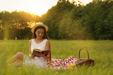 Young woman reading book on picnic blanket in park