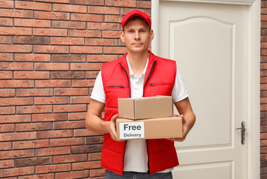 Photo of Courier holding parcels with sticker Free Delivery indoors