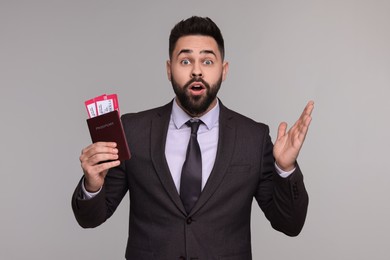 Surprised businessman with passport and tickets on grey background