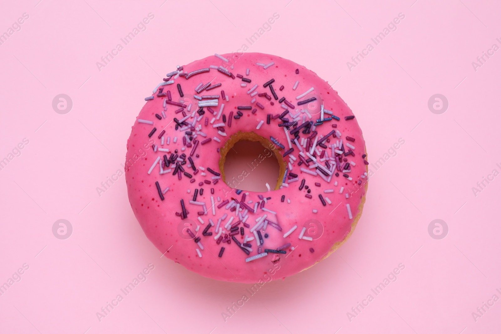 Photo of Glazed donut decorated with sprinkles on pink background, top view. Tasty confectionery