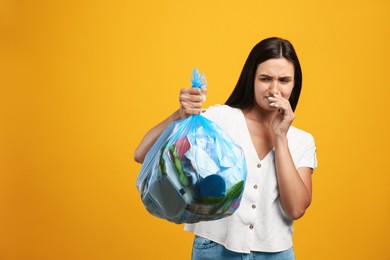 Photo of Woman holding full garbage bag on yellow background. Space for text