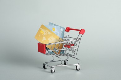 Photo of Small metal shopping cart with credit cards on light background