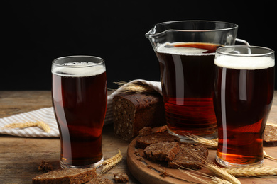 Photo of Delicious kvass, bread and spikes on wooden table against black background