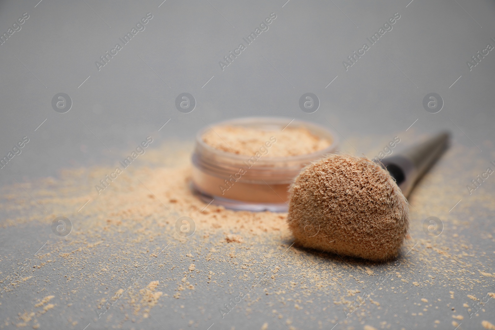 Photo of Loose face powder and makeup brush on light grey background, closeup. Space for text