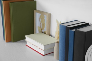 Hardcover books, picture and vase with dry flowers on white wooden table