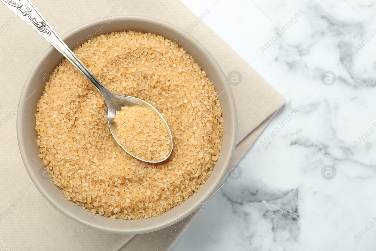 Photo of Brown sugar in bowl and spoon on white marble table, top view. Space for text