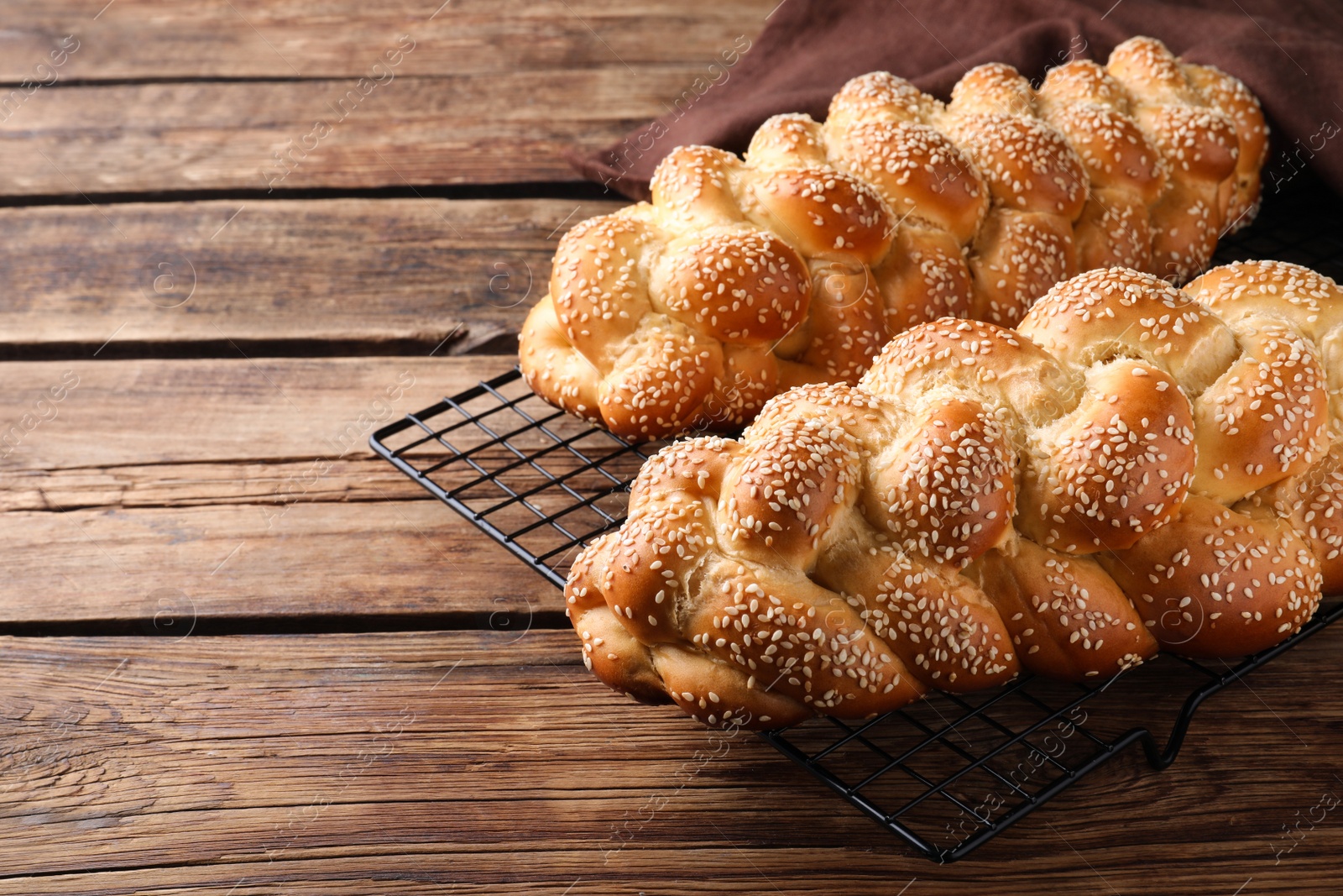 Photo of Homemade braided breads with sesame seeds on wooden table, space for text. Traditional Shabbat challah