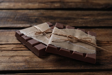 Photo of Tasty milk chocolate bars wrapped in parchment on wooden table