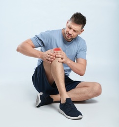 Photo of Full length portrait of man with knee problems sitting on grey background