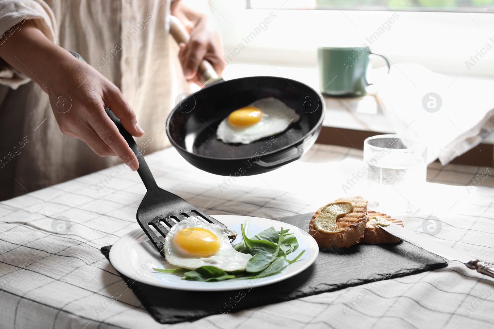 Photo of Woman putting tasty fried eggs onto plate at table indoors, closeup