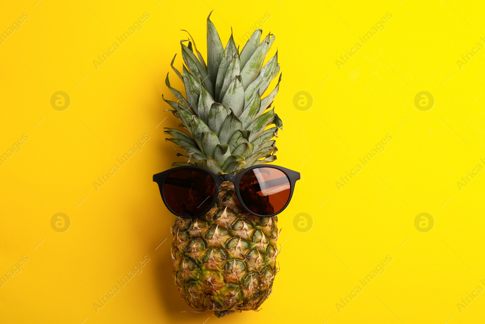 Photo of Pineapple with stylish sunglasses on yellow background, top view
