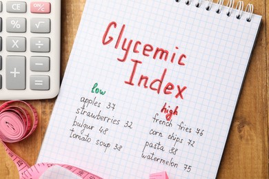 List with products of low and high glycemic index in notebook, calculator and measuring tape on wooden table, flat lay
